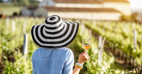 Woman in black and white striped hat holding glass of wine looking at vineyard