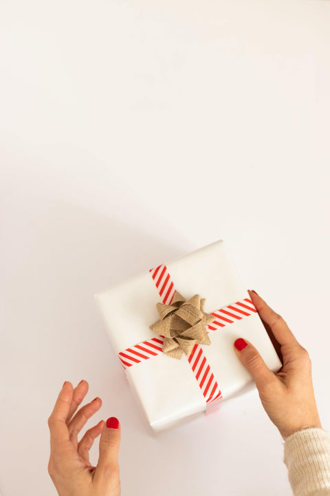 Gift box wrapped in candy-cane striped ribbon with gold  bow and white wrapping paper